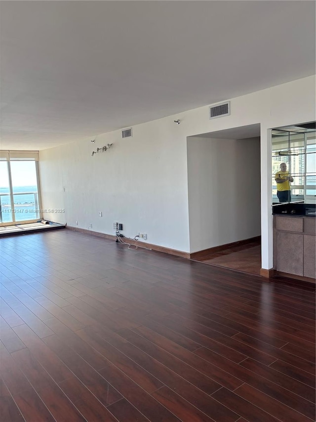 unfurnished room with dark wood-style flooring, visible vents, and baseboards