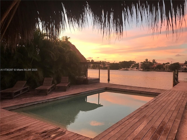 pool at dusk with a water view and a dock