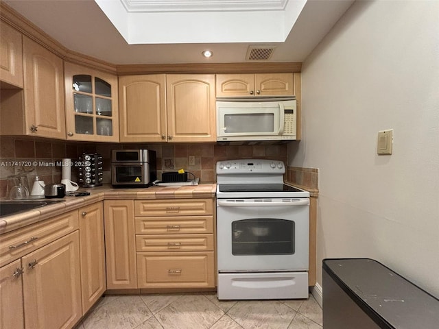 kitchen with white appliances, tile counters, light brown cabinetry, and backsplash