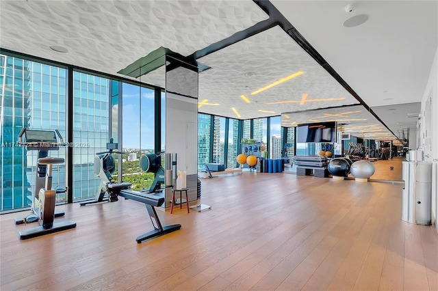 gym featuring floor to ceiling windows, hardwood / wood-style floors, and a textured ceiling