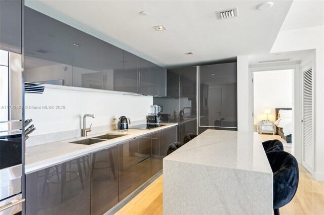 kitchen featuring light hardwood / wood-style flooring, sink, a kitchen breakfast bar, and black electric stovetop