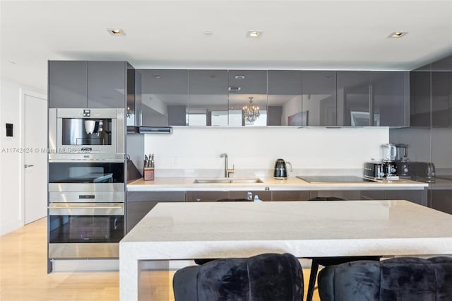 kitchen with sink, gray cabinetry, light hardwood / wood-style floors, stainless steel double oven, and black electric cooktop