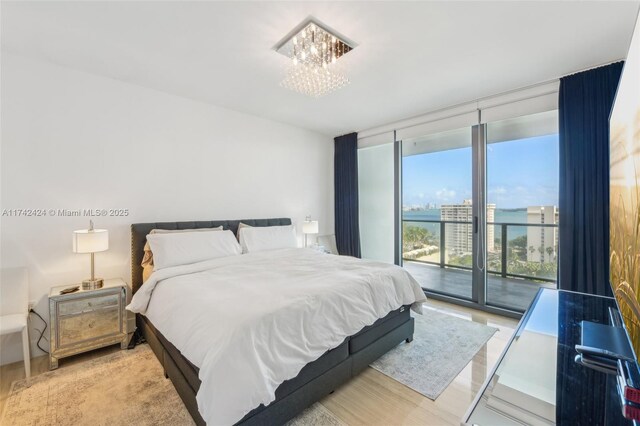 bedroom featuring a notable chandelier, light hardwood / wood-style floors, access to exterior, and a wall of windows