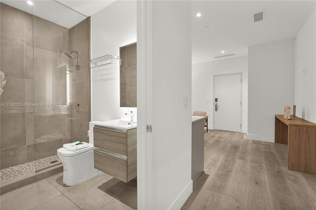 bathroom featuring vanity, hardwood / wood-style floors, toilet, and a tile shower