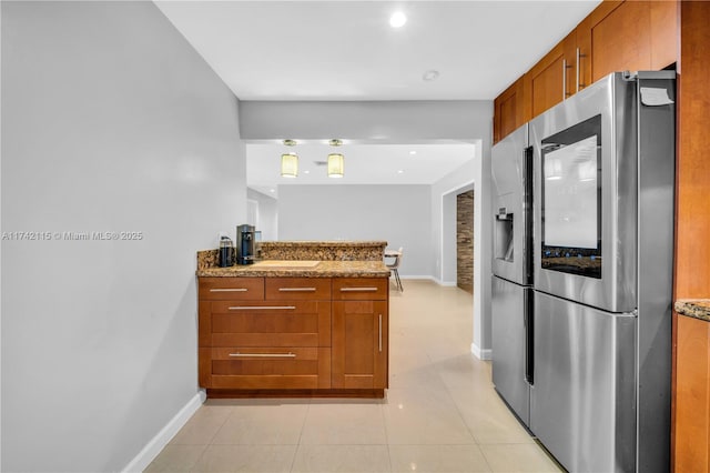 kitchen featuring stainless steel refrigerator with ice dispenser, sink, light tile patterned floors, and stone counters