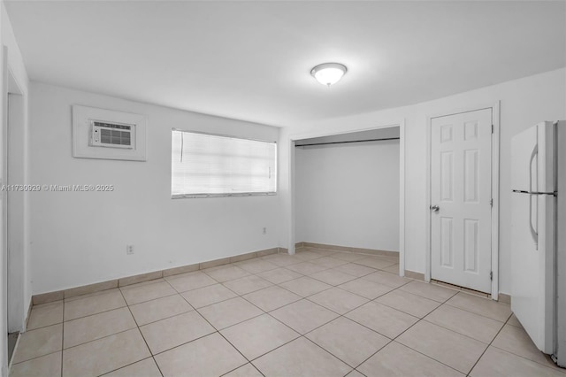 unfurnished bedroom with white refrigerator, an AC wall unit, light tile patterned floors, and a closet