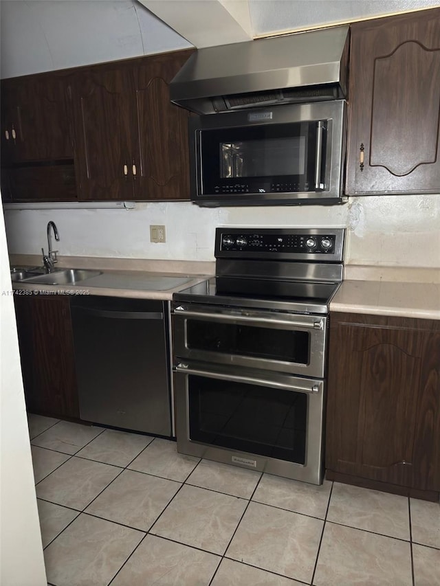 kitchen with light tile patterned flooring, dishwasher, sink, range with two ovens, and dark brown cabinets