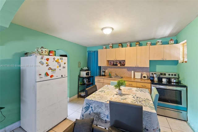 kitchen featuring stainless steel electric stove, light tile patterned floors, white fridge, and light brown cabinets