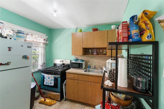 kitchen with white refrigerator, stainless steel range with gas stovetop, sink, and backsplash