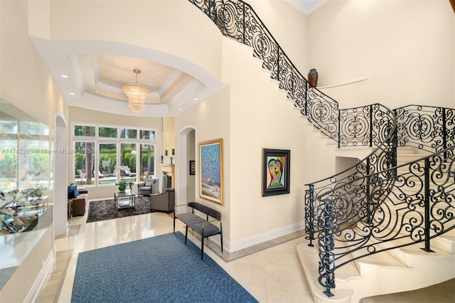 staircase with a high ceiling, crown molding, a notable chandelier, and a tray ceiling