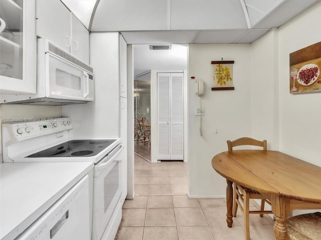 kitchen with a drop ceiling, light tile patterned floors, white appliances, and white cabinets