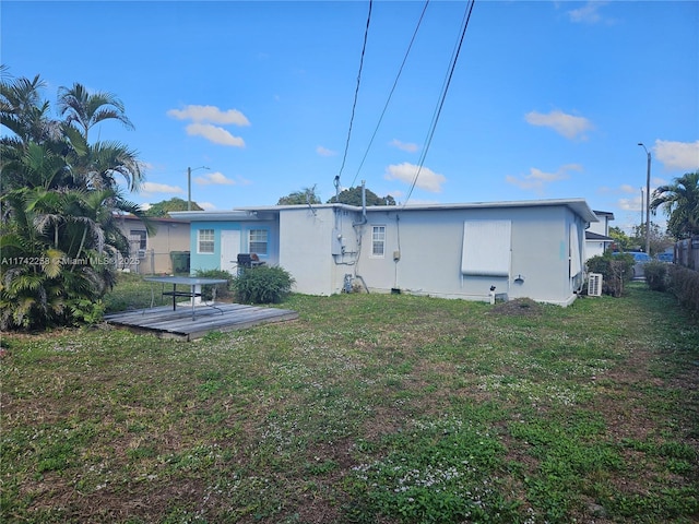 rear view of property featuring stucco siding, a lawn, fence, and a wooden deck