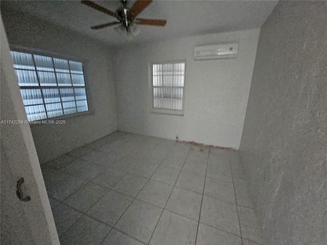 empty room featuring ceiling fan, a wall mounted air conditioner, tile patterned flooring, and plenty of natural light