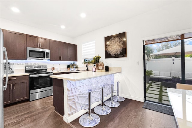 kitchen with a breakfast bar, sink, dark hardwood / wood-style flooring, kitchen peninsula, and stainless steel appliances