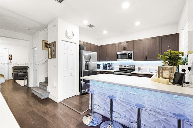 kitchen featuring a breakfast bar area, dark wood-type flooring, kitchen peninsula, stainless steel appliances, and dark brown cabinets