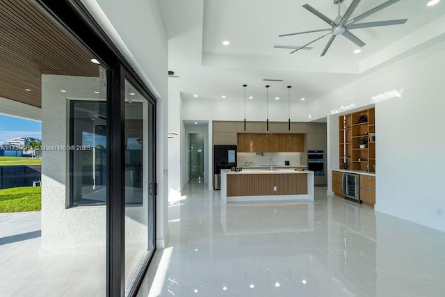 kitchen featuring a kitchen island, decorative light fixtures, beverage cooler, a high ceiling, and a raised ceiling