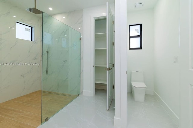 bathroom featuring plenty of natural light, a tile shower, and toilet