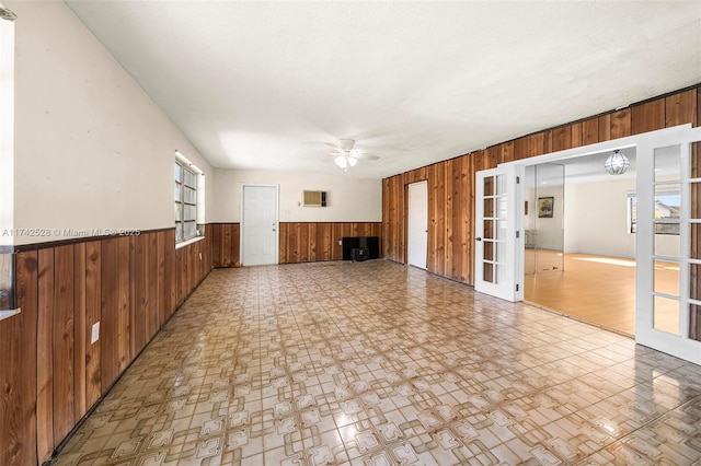 unfurnished living room with ceiling fan, a textured ceiling, wooden walls, and french doors