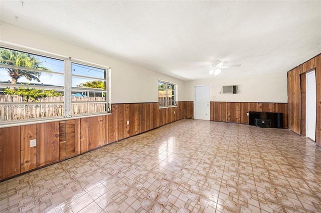 unfurnished living room featuring ceiling fan, wooden walls, and a textured ceiling