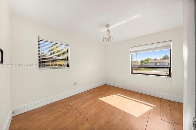 spare room with hardwood / wood-style floors and an inviting chandelier