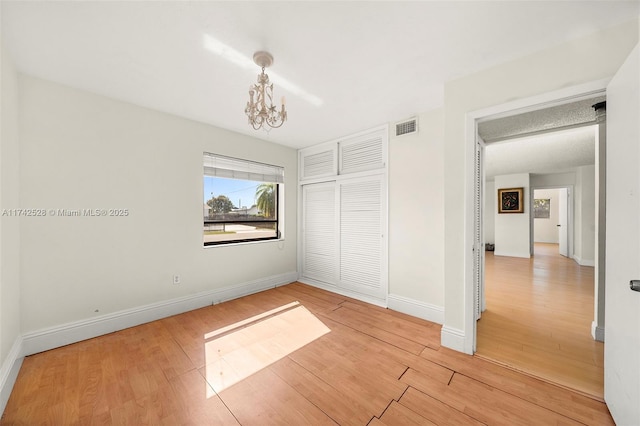 unfurnished bedroom with a notable chandelier, light wood-type flooring, and a closet