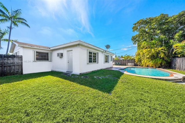 back of property with a fenced in pool, a wall unit AC, and a lawn