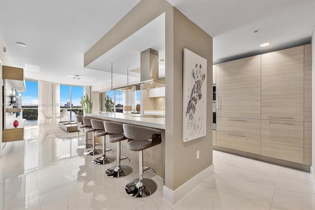 kitchen with floor to ceiling windows, island range hood, a kitchen bar, decorative light fixtures, and kitchen peninsula