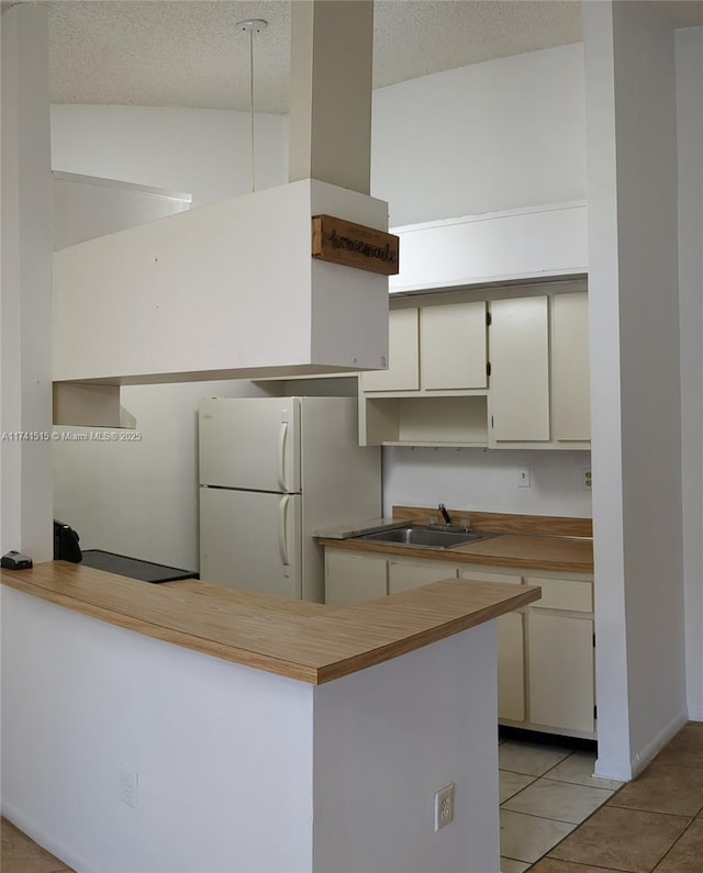 kitchen featuring sink, light tile patterned floors, white cabinets, kitchen peninsula, and white fridge