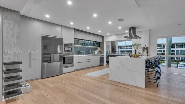 kitchen with a breakfast bar area, light hardwood / wood-style floors, stainless steel built in fridge, and island exhaust hood