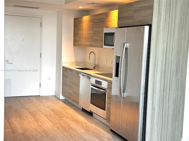 kitchen with appliances with stainless steel finishes, sink, and light hardwood / wood-style flooring