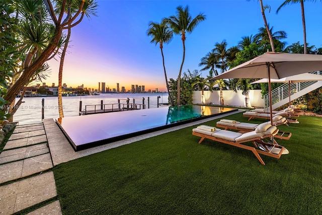 pool at dusk featuring a water view and a lawn