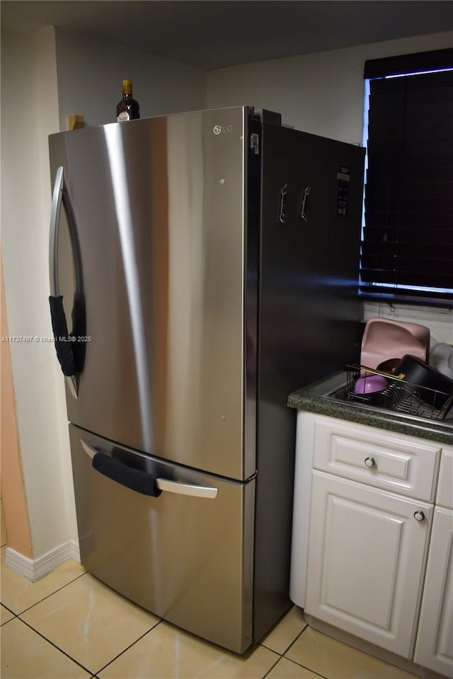 kitchen with light tile patterned floors, stainless steel refrigerator, and white cabinets