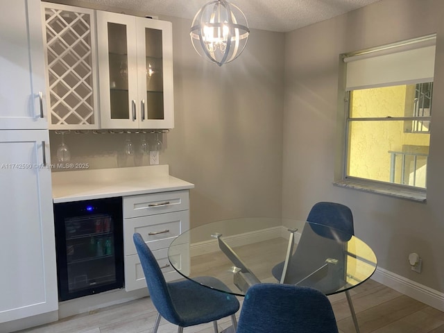 dining area with indoor bar, wine cooler, light hardwood / wood-style floors, a textured ceiling, and an inviting chandelier