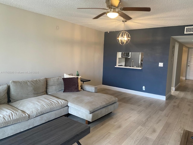 living room featuring ceiling fan with notable chandelier, light hardwood / wood-style floors, and a textured ceiling