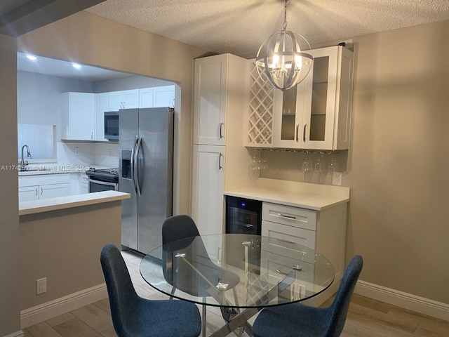 kitchen with white cabinetry, wine cooler, hanging light fixtures, stainless steel appliances, and light wood-type flooring