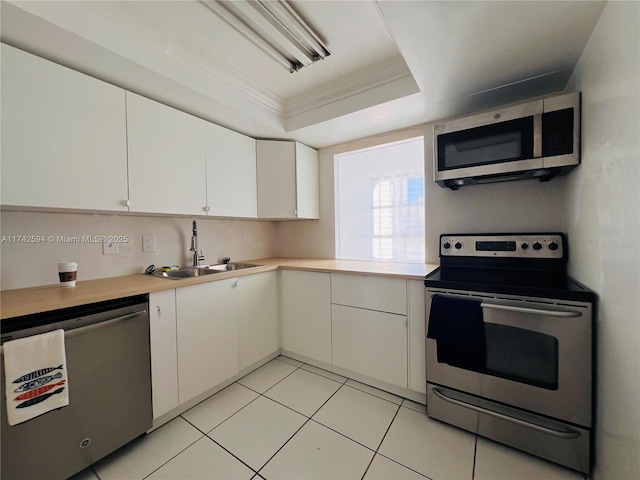 kitchen with a tray ceiling, light countertops, appliances with stainless steel finishes, ornamental molding, and white cabinets