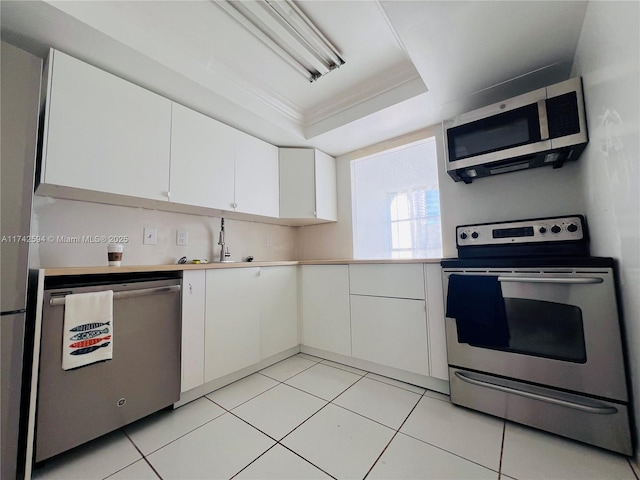 kitchen featuring white cabinetry, light countertops, appliances with stainless steel finishes, a tray ceiling, and crown molding