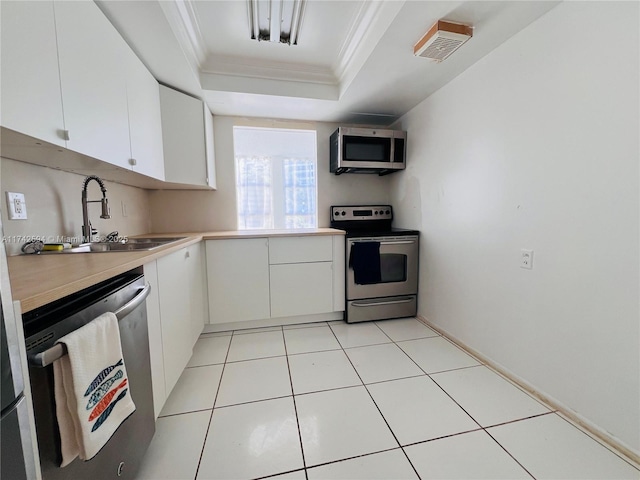 kitchen featuring appliances with stainless steel finishes, sink, white cabinets, ornamental molding, and a tray ceiling