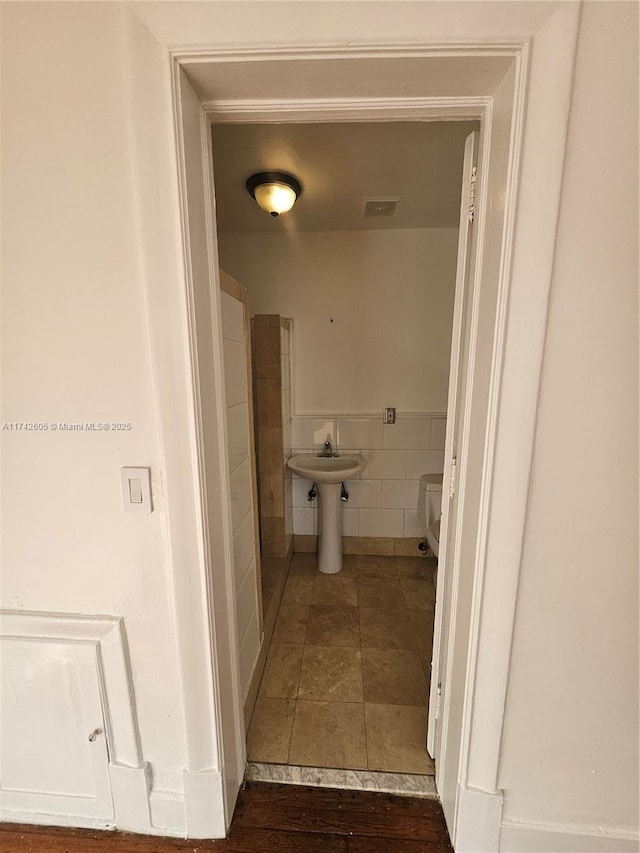 bathroom with toilet, sink, and tile walls