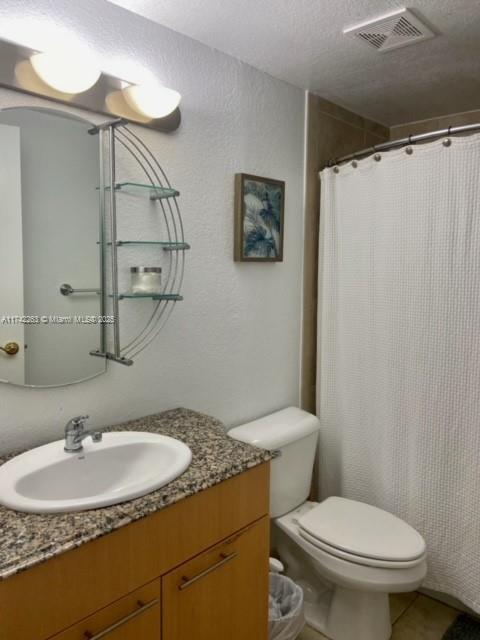 bathroom featuring vanity, tile patterned flooring, a textured ceiling, and toilet