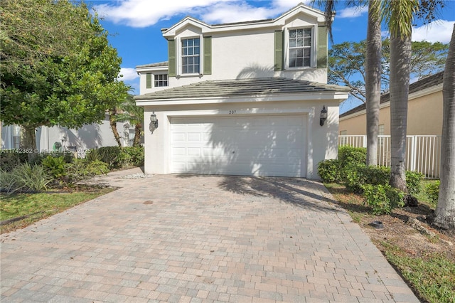 traditional home with a tile roof, an attached garage, fence, decorative driveway, and stucco siding