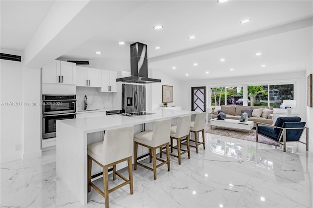 kitchen with island range hood, white cabinetry, a breakfast bar area, stainless steel appliances, and a spacious island