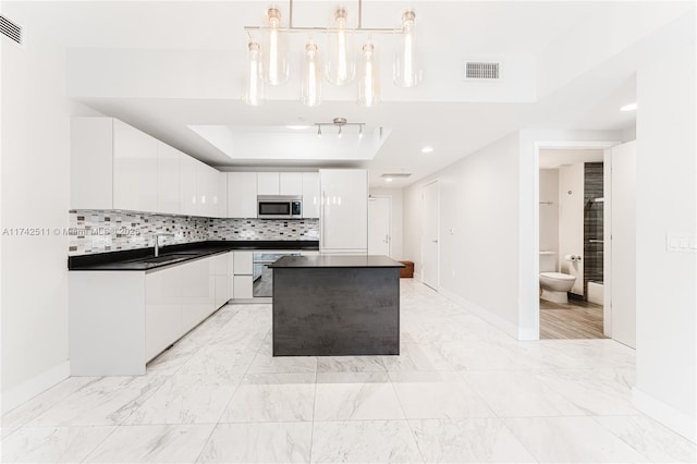 kitchen featuring white cabinetry, hanging light fixtures, a tray ceiling, oven, and backsplash