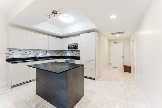 kitchen with white cabinetry, backsplash, a tray ceiling, and a center island