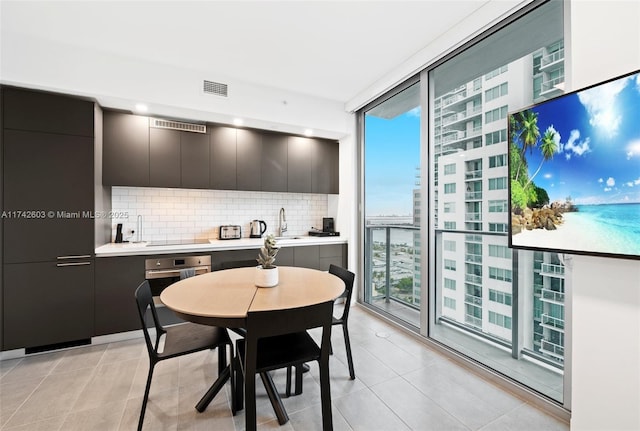 kitchen featuring backsplash, floor to ceiling windows, black electric stovetop, light tile patterned flooring, and oven