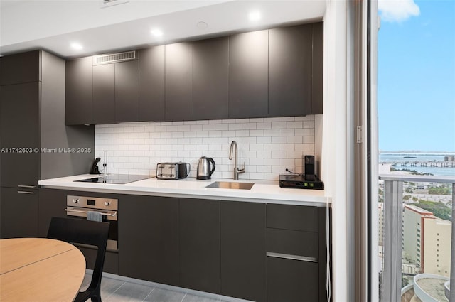 kitchen featuring black electric cooktop, oven, sink, and decorative backsplash