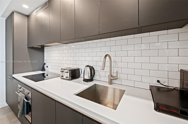 kitchen featuring sink, gray cabinets, tasteful backsplash, black electric stovetop, and oven