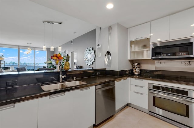 kitchen with dark countertops, modern cabinets, white cabinetry, a sink, and appliances with stainless steel finishes