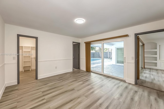 empty room with built in shelves and light hardwood / wood-style floors