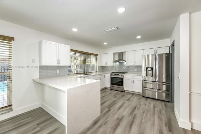 kitchen with appliances with stainless steel finishes, white cabinets, light hardwood / wood-style floors, and wall chimney exhaust hood